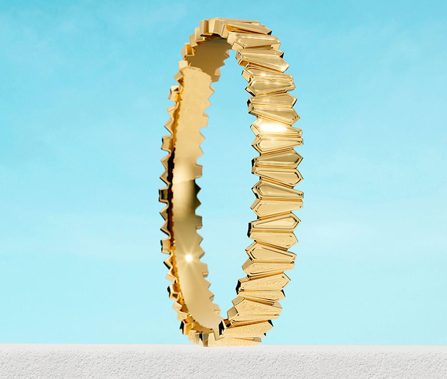 Birks Beekeeper yellow gold bangle bracelet on a blue background.